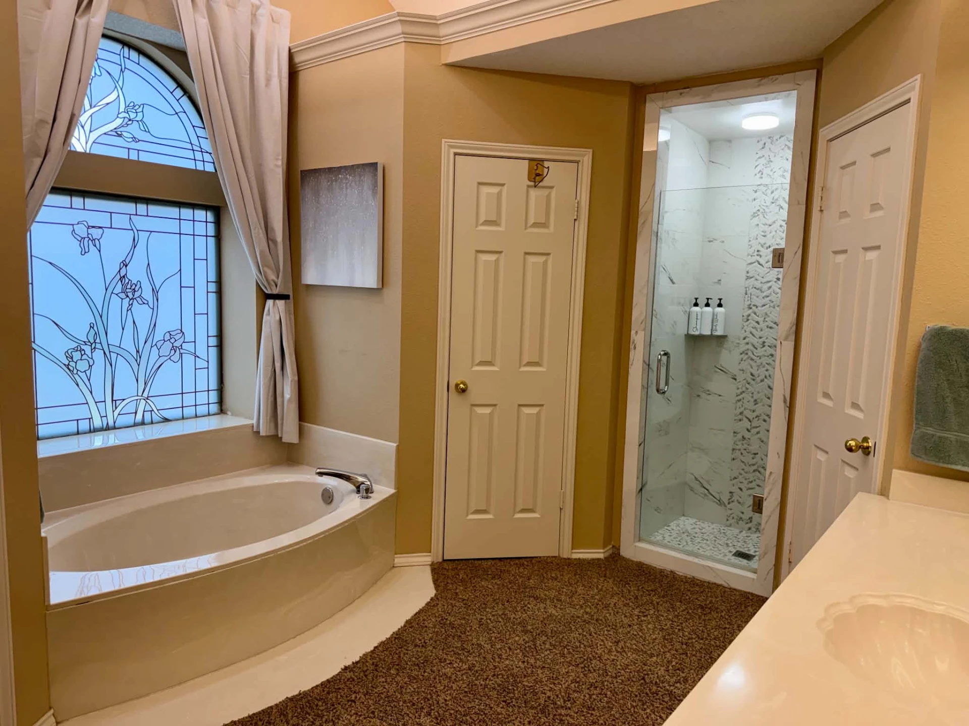 Primary bathroom — soaker tub beneath an arched stained-glass window, with a separate glass-enclosed walk-in shower