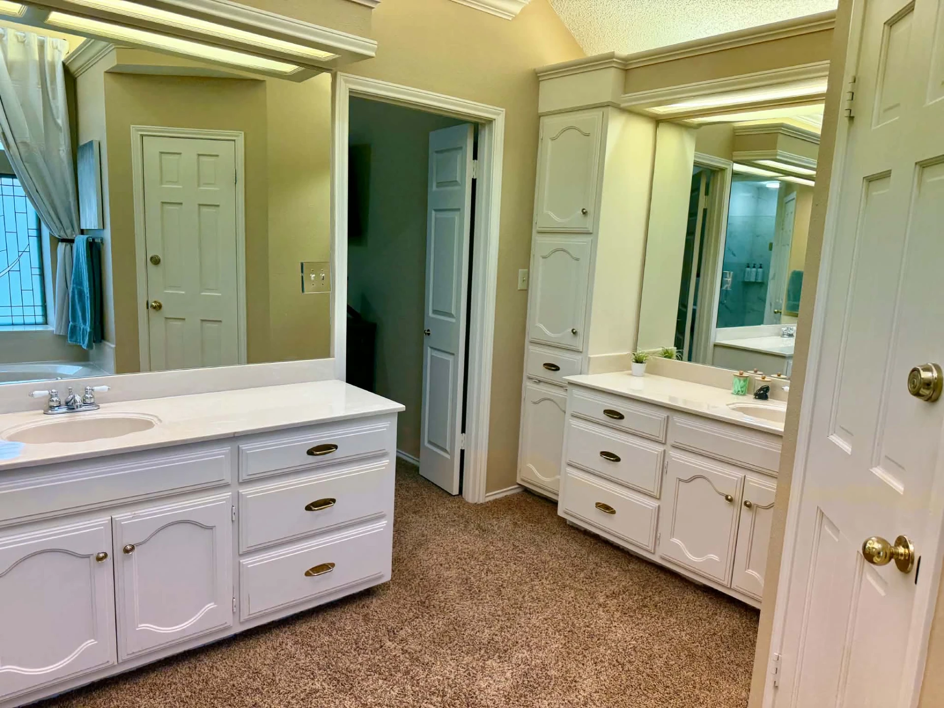 Primary bathroom — dual white vanities with large mirrors and a linen storage tower